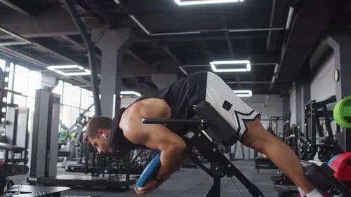 Man with Headphones Trains Back Muscles and Abs in Gym Side View