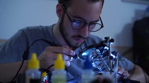 Porträt eines erfolgreichen jungen bärtigen Mannes in Brille, der bei seiner Arbeit mit einem Lötkolben arbeitet