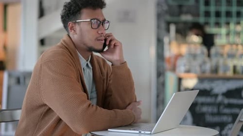 Young Adult Working on Laptop Answering Cell Phone
