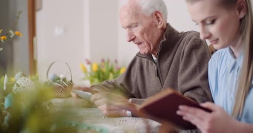 Elderly Man and Young Woman Read Together Indoors