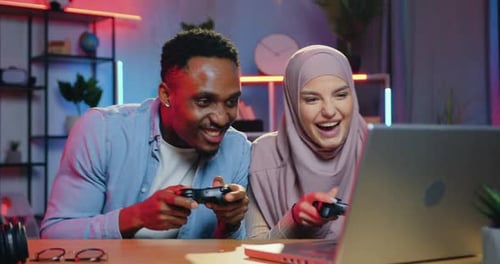 Un chico de piel negra celebra la victoria en un videojuego sobre su pareja árabe