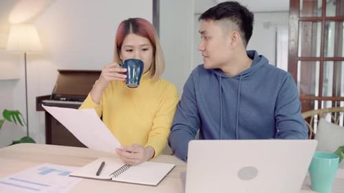 Young couple managing finances, reviewing their bank accounts using laptop and calculator at home.