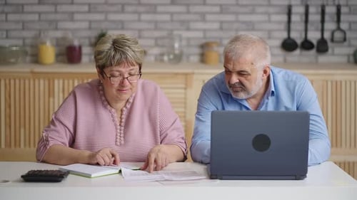 Couple Reviews Finances Using Laptop at Kitchen Table
