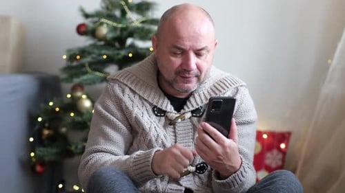 Man Uses Phone in Front of Christmas Tree