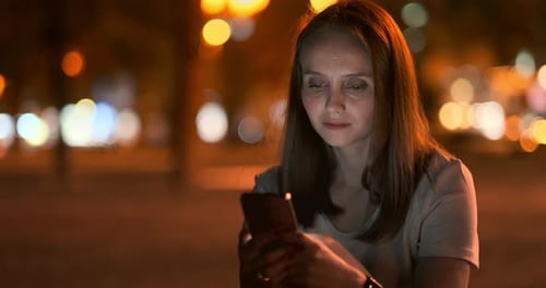 Young Girl in the Night City Writes Text Messages in a Smartphone