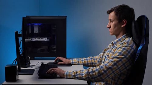 Mann spielt Videospiel auf einem großen Computerbildschirm und sitzt auf einem Gaming-Stuhl in einem halbdunklen Raum, beleuchtet von