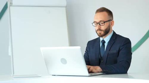 Attractive Businessman in Suit and Glasses Working with Laptop in White Office