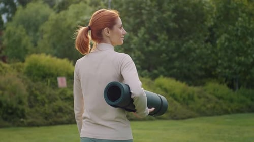 Back view of caucasian woman going joyful in the park to do yoga.