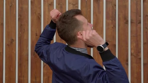 Divertido hombre barbudo baila en un fondo de pared de madera con movimientos divertidos