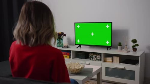 Woman watching TV focused eating popcorn. Green Screen TV Chroma Key.