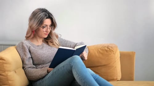 Woman Reading Book on Yellow Couch Indoors