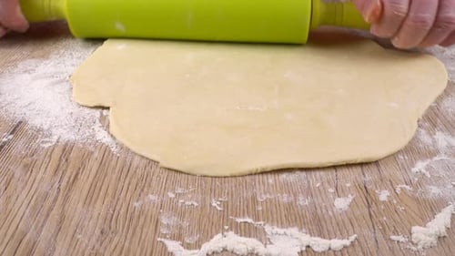 Hands Roll Dough With Rolling Pin on Wooden Surface