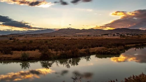 Time lapse of a cloudscape reflecting off a glassy river at sunset with mountains in the distance