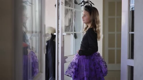 Encantadora niña caucásica feliz con disfraz de Halloween y diadema de murciélago de pie en interiores