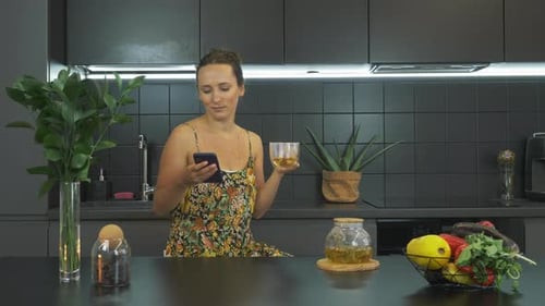 Woman Uses Smartphone and Drinks Tea at Home