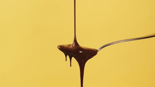 Pouring Chocolate Sauce on Spoon with Yellow Background