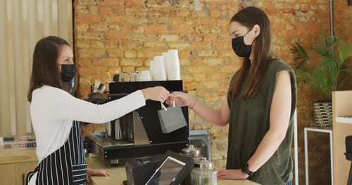 Caucasian waitress wearing face mask giving take-away order to caucasian female customer
