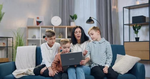 Madre explicando cómo usar la computadora portátil a sus tres hijos interesados de diferentes edades
