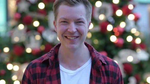 Feliz joven guapo contra árboles de navidad iluminados al aire libre