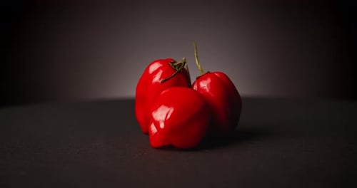 Three Shiny Red Peppers Rotating on Dark Surface