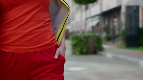 a Woman's Body in Red Clothes Has Put Hand in Pocket and is Walking Along a City Street