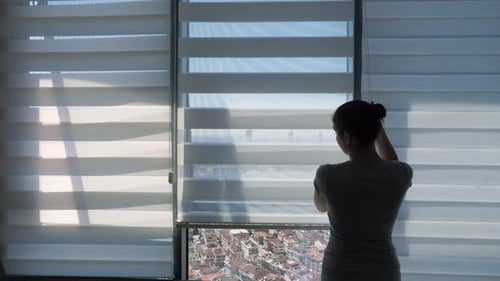 Woman Is Opening Blinds, Looking at Window with Panoramic City View and Stretching.