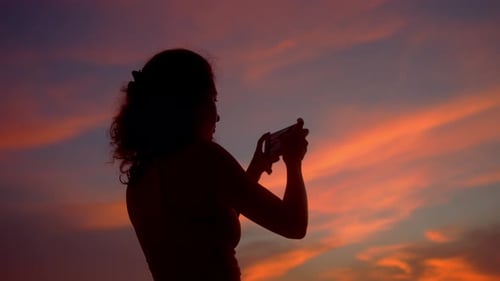Woman Silhouetted Taking Pictures at Beautiful Sunset