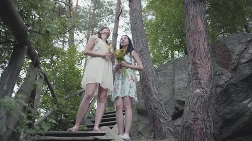Women Friends Holding Flowers Stand on Forest Steps