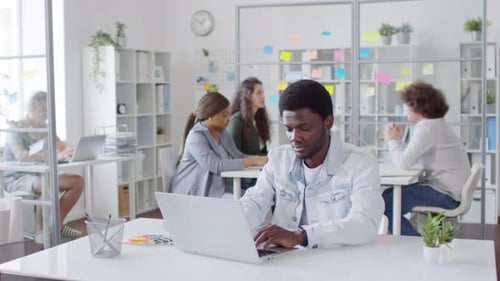 African American Man Typing on Laptop and Smiling at Camera in Office