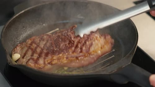 Steak cooking in cast iron skillet with garlic