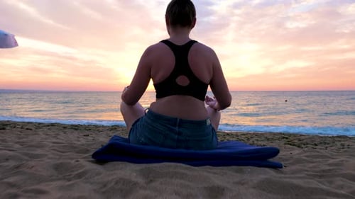 Woman Sits on the Beach Practicing Yoga at the Sunrise