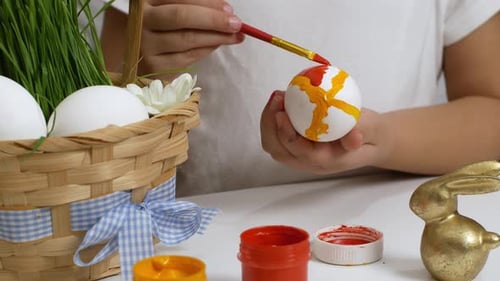 Children drawing on painted eggs at the table, at home. Preparing for the Easter holiday.