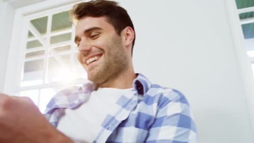 Smiling Man Using Phone in a Bright Living Room