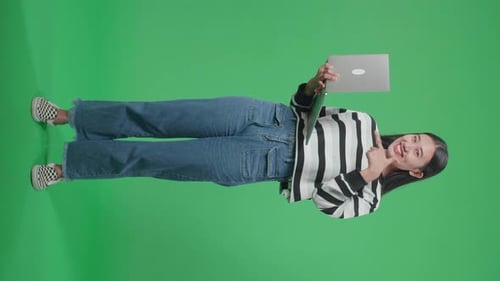 Full Body Of A Smiling Asian Woman Pointing To Computer While Standing In Front Of Green Screen