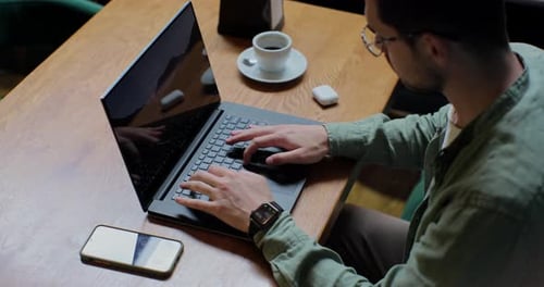 Top View of Man in Casual Clothes is Typing on a Laptop Sitting at a Table