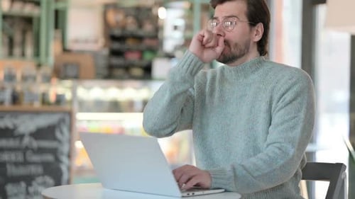 Man Coughs While Using Laptop in Cafe
