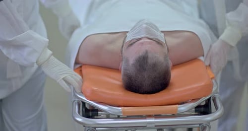 Doctors Carry a Sick Man on a Stretcher Along the Hospital Corridor