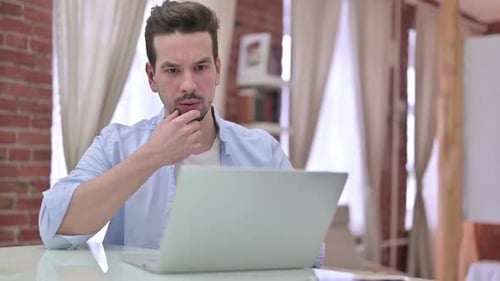 Junger Mann denkt und arbeitet am Laptop