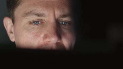 Man Looking at Computer Screen in Dark Room