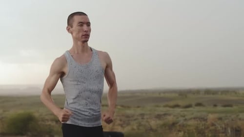 Muscular Athlete Runs Through Countryside During Light Rain Front View