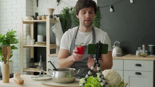 Jeune chef en tablier se filme pour un blog de cuisine tout en préparant un repas sain avec