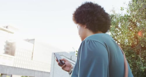 Plus size biracial woman walking on stairs with smartphone in city