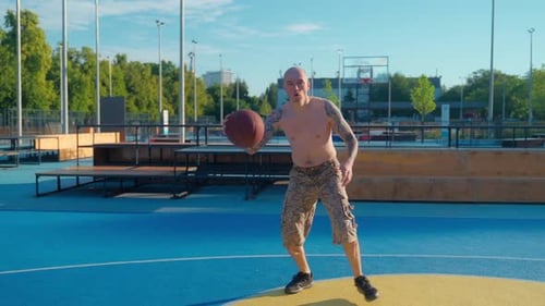 Shirtless Man Practices Basketball Skills on Outdoor Court