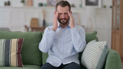 Man with Headache Rubbing Temples on Couch