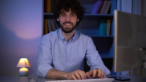 Man Typing at Computer Desk Smiling at Camera