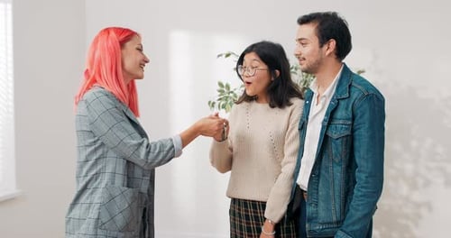 A Real Estate Agent Hands Young Couple in Love Keys to Their Newly Purchased Apartment Woman is