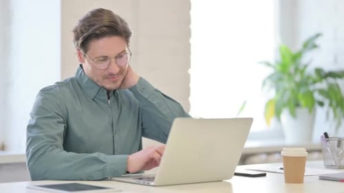 Man Working on Laptop in Office Rubs Neck