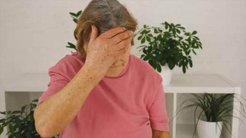 Senior Woman Holds Pills, Places Hand on Forehead