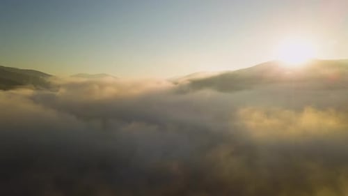 Luftaufnahme eines lebhaften Sonnenaufgangs über weißem dichtem Nebel mit fernen dunklen Silhouetten eines Berges