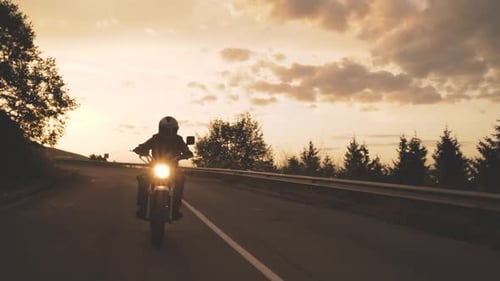 Silhouette of a Biker on Classic Motorcycle Driving Off the Sunset in the Mountains